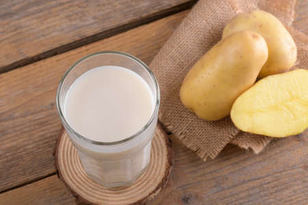 Vegan potato milk and potato on rustic wooden background. Plant based alternative milk replacer and lactose freeの写真素材
