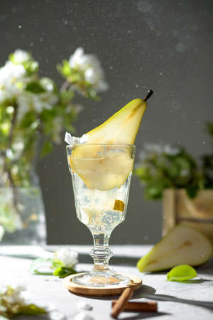 Pear cocktail with pear puree and fresh fruit and flowers on light gray background. Summer cold pear drink lemonade with ice on the table, Sparkling Mocktail dessert beverage with flowering twigsの写真素材