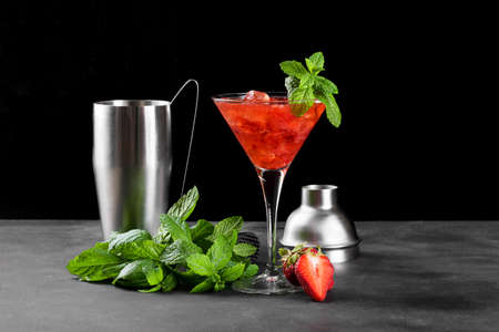 Cold summer strawberry cocktail mojito, margarita, daiquiri in a martini glass. Fresh strawberry drink with ice, bartender tools set and mint leaves on dark background. Iced strawberry lemonadeの写真素材