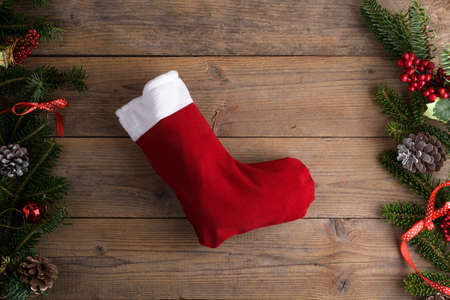Red Christmas stockings on a rustic wooden wall background with Christmas decoration, fir tree and cone, red ribbon. Epiphany Befana's stockings or Santa Claus stocking for sweetの写真素材