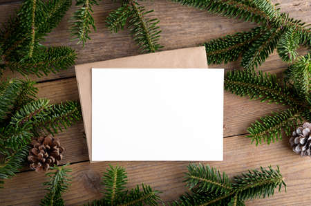 Christmas 7x5 card mockup template with envelope with fir twigs and Christmas decor on wooden background. Design element for Christmas and New Year congratulation, greeting or invitation cardの写真素材
