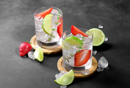 Fresh strawberry mojito cocktail. Two glasses with cold summer strawberry soda drink with strawberry, ice cubes and lime, decorated wiht thyme on dark background. Iced strawberry lemonade, close upの写真素材