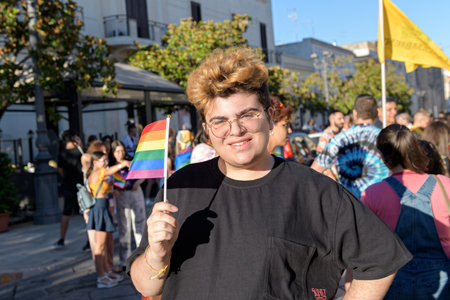 Manduria, Italy - JULY, 13, 2022 A beautiful guy with LGBT flag smiling and looking in camera during the Gay Pride march. LGBTQ Pride Day Celebrations in the streetのeditorial素材