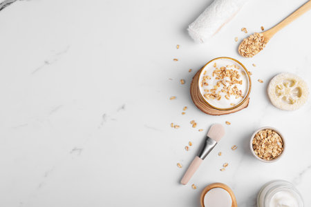 Homemade facial mask or creamy scrub with cereal, made of yogurt and oats flake, home spa cosmetics on a white marble background with natural beauty treatment ingredients and towel, flat lay, top viewの写真素材