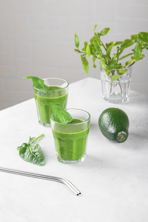 Healthy green smoothie with spinach, avocado, banana, and vegan milk in two glasses and fresh ingredients on light gray table background. Detox, diet, healthy, vegetarian food conceptの写真素材