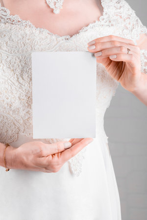 Woman wearing a wedding dress holding wedding stagionery invitation card mockup 5x7 on white wall backgroundの写真素材
