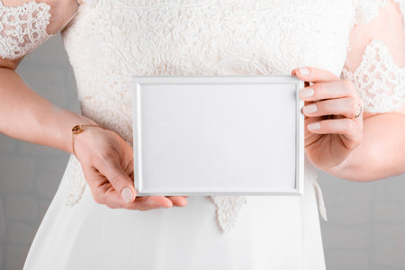 Woman wearing a wedding dress holding wedding stagionery invitation card mockup 7x5 on white wall backgroundの写真素材