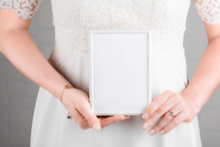 Woman wearing a wedding dress holding wedding stagionery invitation card mockup 7x5 on white wall backgroundの写真素材