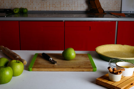 One green apple on a cutting board and kitchen knife on a table with ingredients for apple pie: green apples, cinnamon sticks and raw crust pie dough. Cooking homemade Thanksgiving fruit autumn tartの写真素材