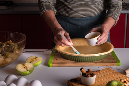 Woman's hands spreading eggs on the dough with a cooking brush in a bakery dish, apple pie making, Thanksgiving tart preparation, autumn bakery, lifestyle, fall sweets, recipeの写真素材