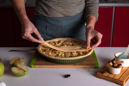 Woman placing pie dough on top of the apple pie in the bakery dish, ready to be put in the oven, preparing apple pie. Thanksgiving tart preparation, autumn bakery. Crispy weather sweets. Recipeの写真素材