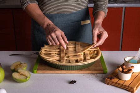 Woman placing pie dough on top of the apple pie in the bakery dish, ready to be put in the oven, preparing apple pie. Thanksgiving tart preparation, autumn bakery. Crispy weather sweets. Recipeの写真素材
