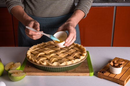 Woman spreading eggs on the raw apple pie with a cooking brush in a bakery dish, recipeの写真素材
