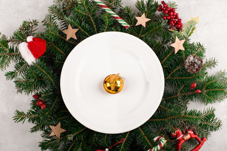 Christmas table setting with gold decoration on white plate on natural fir branches background. Christmas festive decoration serving for Christmas dinner, flat lay, top viewの写真素材