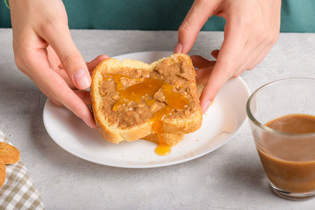 Female hands holding a sandwich with honey and peanut butter spreading on piece of white bread...