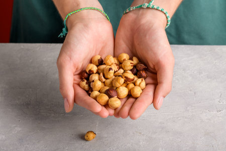 Woman holding peeled whole hazelnuts in her hands at gray table, closeup. Handful of dried hazelnuts...