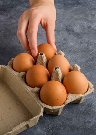 A woman's hand takes an egg from the egg box that is on the gray kitchen table, close up, food...