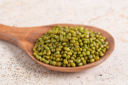 Mung beans in a wooden spoon on beige kitchen table backgroundの写真素材