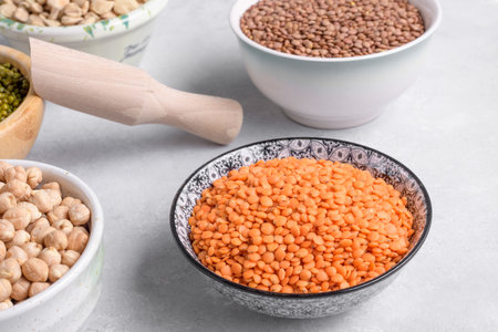 Raw red lentils in ceramic bowl and mixed pulses on gray tableの写真素材