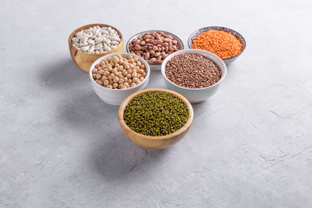 Mixed legumes for vegetarian and vegan cooking on gray table. Red lentins, White beans, green mung beans, cranberry beans in the bowls, pulses for healthy balanced diet, plant-based protein sourceの写真素材