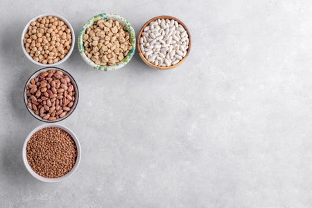 Mixed legumes for vegetarian and vegan cooking on gray table. Lentils, white beans, chickpeas, cranberry beans in the bowls, pulses for healthy balanced diet, plant-based protein sourceの写真素材