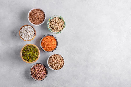 Mixed legumes for vegetarian and vegan cooking on gray table. Red lentins, White beans, green mung beans, cranberry beans in the bowls, pulses for healthy balanced diet, plant-based protein sourceの写真素材