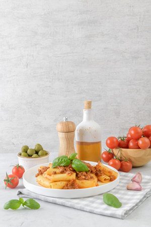 Rigatoni pasta with rich Bolognese sauce and basil garnish on light gray table backgroundの写真素材