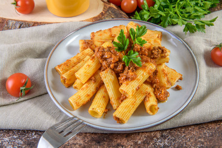 Rigatoni pasta with homemade bolognese ragu sauce on linen napkin served on rustic style brown tableの写真素材
