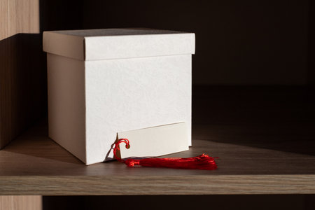 White Box and Blank card with Red Tassel Displayed on Wooden Shelfの写真素材
