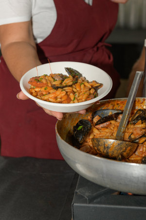 A chef in an apron presents a plate of pasta with seafood during food festival in Pugliaの写真素材