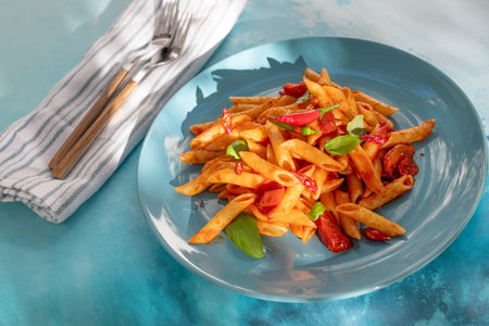 Classic penne all'Arrabbiata with chili, and tomato flavor on ceramic blue plate on blue kitchen table on sunny dayの写真素材