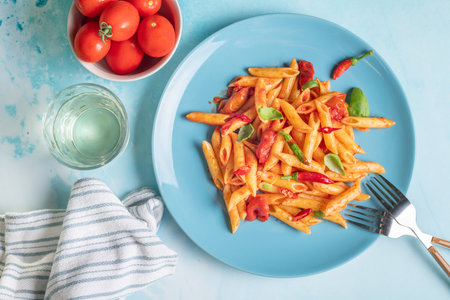 Italian comfort lunch food penne all'Arrabbiata with basil and red chili on ceramic blue plate on blue kitchen table on sunny dayの写真素材
