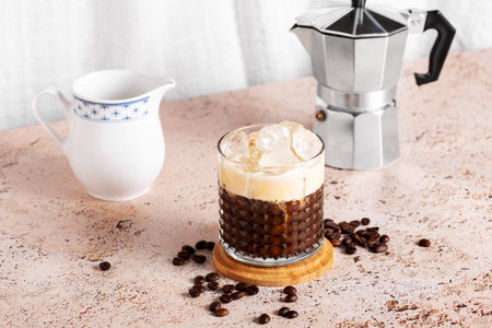 Iced creamy coffee into a glass with moka pot and milk jug on beige kitchen tableの写真素材