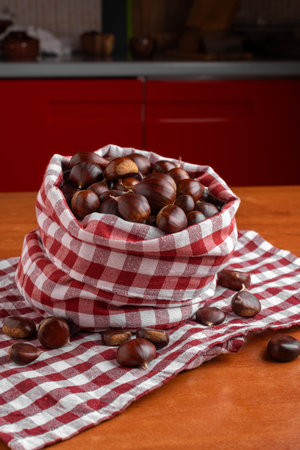 Fresh chestnuts in a red checkered cloth bag on a wooden kitchen tableの写真素材