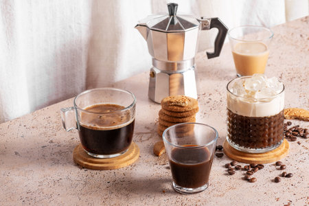 Freshly brewed espresso, iced coffee and moka pot in beige cozy kitchen setup. Different types of coffee drinks with cookies on a beige tableの写真素材