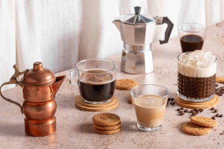 Freshly brewed espresso, iced coffee and two moka pots in beige cozy kitchen setup. Different types of coffee drinks with cookies on a beige tableの写真素材