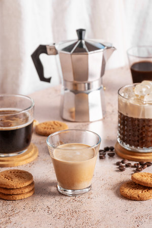 Variety of coffee drinks with moka pot and cookies on warm background. Coffee with milk, classic espresso and iced coffee with cookies on beige textured countertopの写真素材