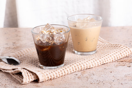 Two coffee drinks, iced latte and black espresso on beige stone textured backgroundの写真素材