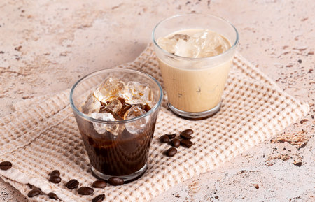 Iced coffee and black coffee served in clear glasses on beige stone table, close upの写真素材