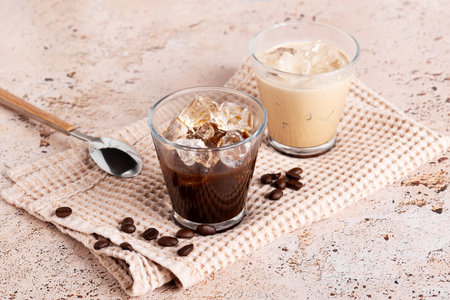 Pair of coffee glasses with iced drink and strong black coffee on beige stone kitchen tableの写真素材
