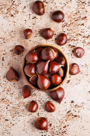 Wooden bowl filled with chestnuts on beige stone kitchen table, autumn seasonal food themes, top viewの写真素材