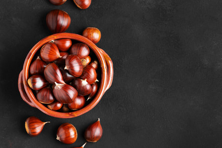 Raw chestnuts in a rustic clay bowl on black background, web banner, copy spaceの写真素材