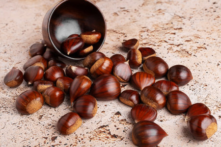 Autumn raw chestnuts in rustic wooden bowl on beige stone kitchen table background, close upの写真素材