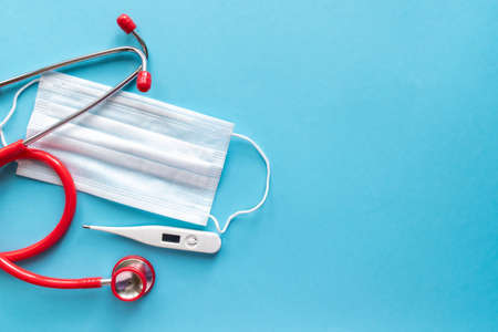 Medical equipment: red stethoscope, thermometer and mask on a light blue background with a place for text. Copy space. Medical concept.の写真素材
