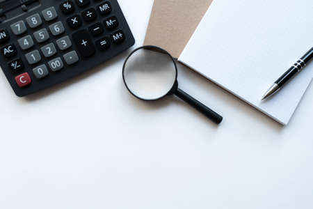 Workplace with notebooks, magnifying glass, calculator and pen on light white backround. Copy space. Close up. Top view. Concept business.の写真素材