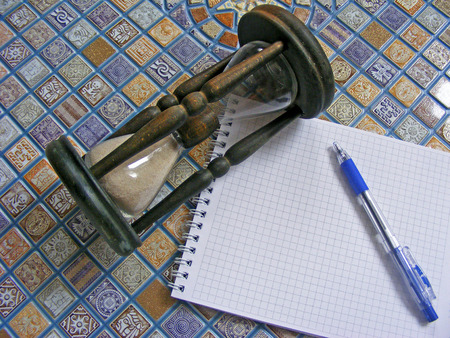 Wooden hourglass, pen and agenda on the mosaic backgroundの写真素材