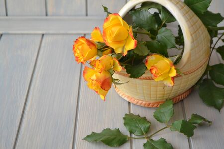 Bright orange and yellow little roses in a ceramic basket on blue wooden tableの写真素材