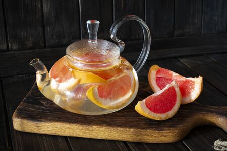 Pink grapefruit herbal tea with ginger and honey in a glass teapot on wooden tableの写真素材