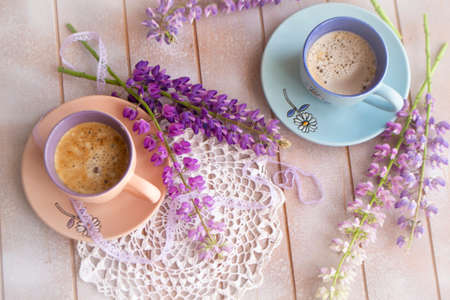 Pink and purple lupine flowers and cup of coffee on a old wooden shabby table