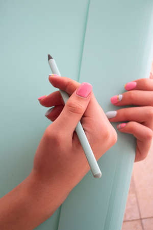 Closeup image woman hand with pencil on teal backgroundの写真素材